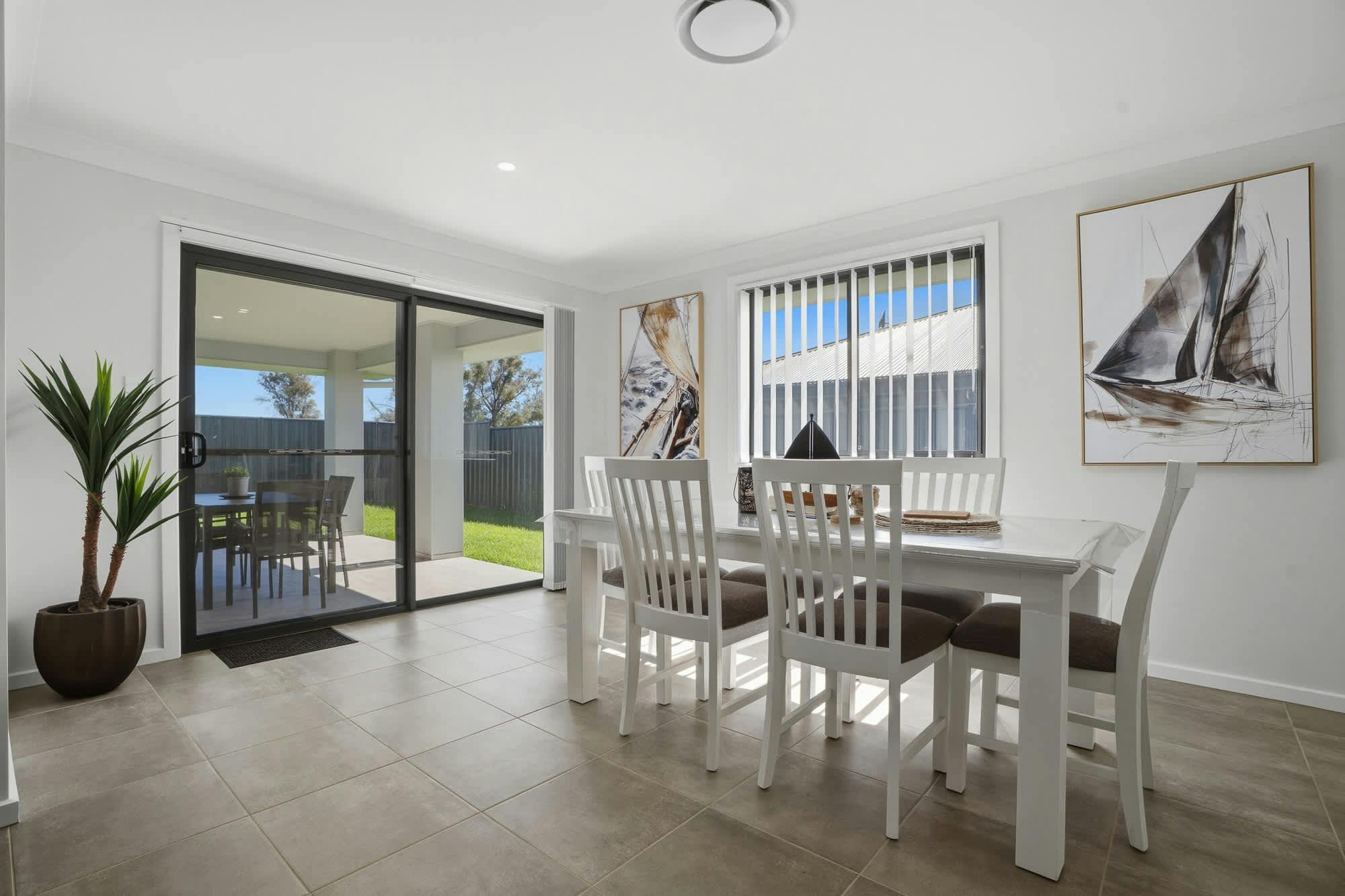 White dining table and chairs with artwork and large glass sliding door going to ourdoor setting.