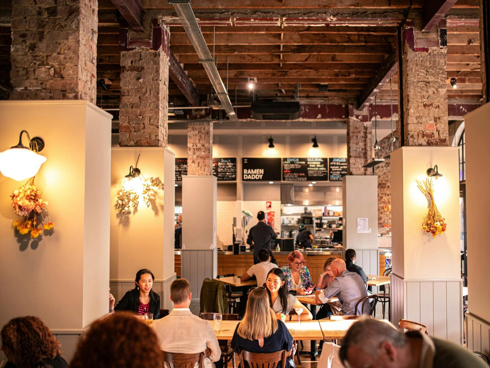 Food hall with people sitting beside columns with lights and dried flowers