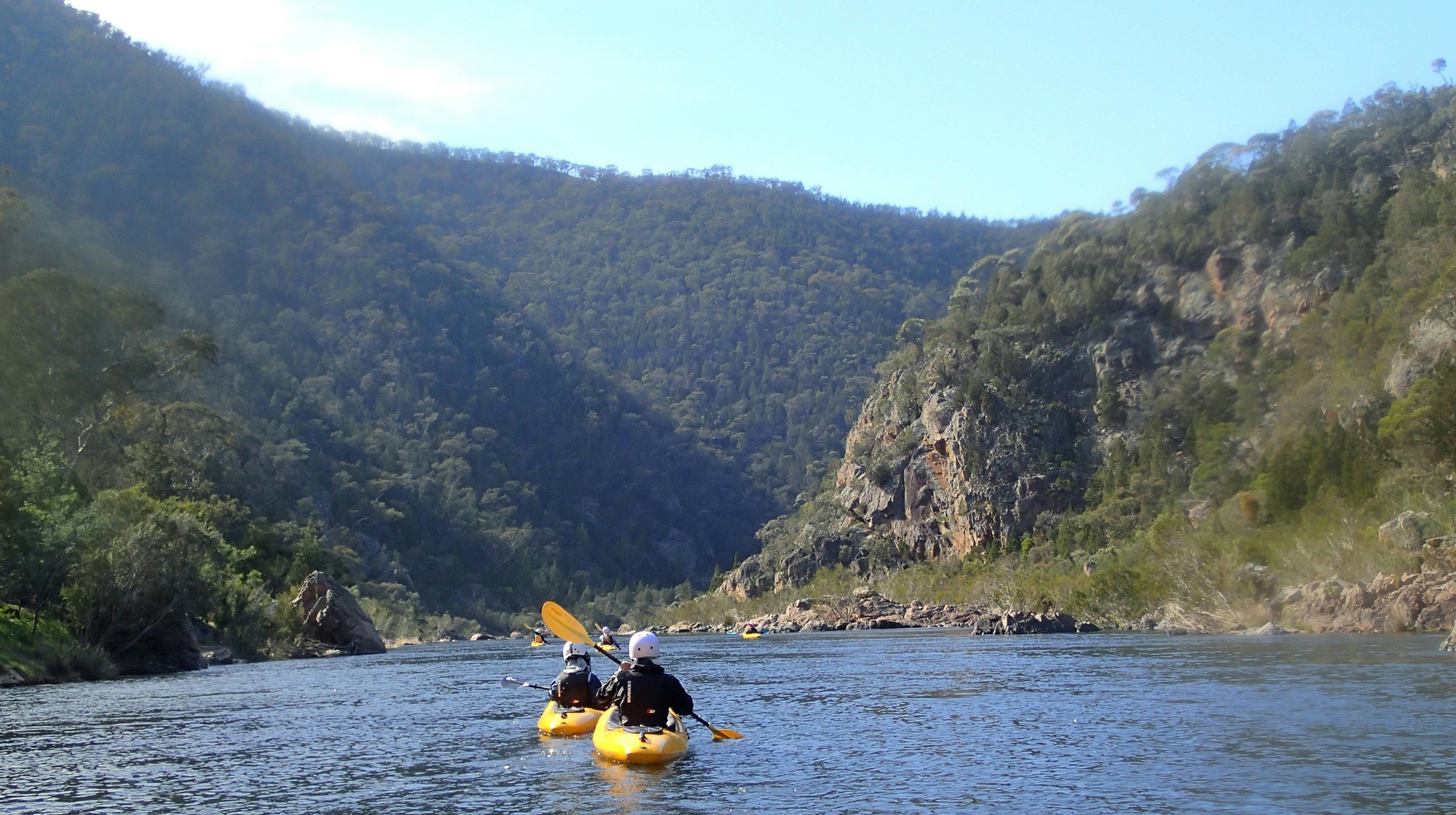 a view of mountains with the snowy river and two kayakers paddling in the foreground