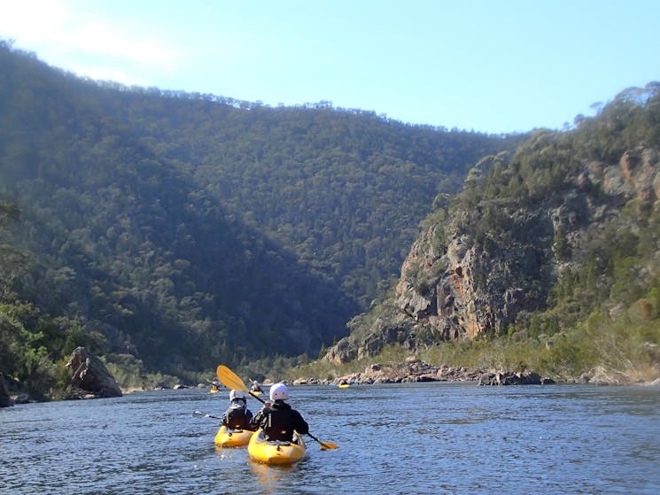 a view of mountains with the snowy river and two kayakers paddling in the foreground