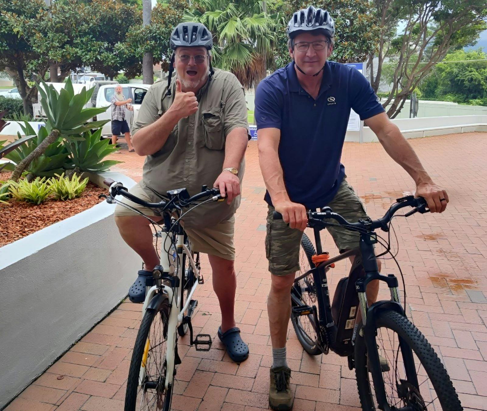 Two male customers, helmets on, thumbs up, ready to explore on their ebikes