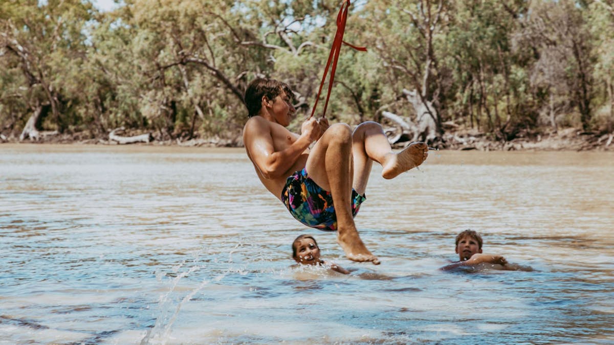 Young boy swinging into the water at the Goondiwindi Water Park while his brothers watch on Young boy swinging into the water at the Goondiwindi Water Park while his brothers watch on