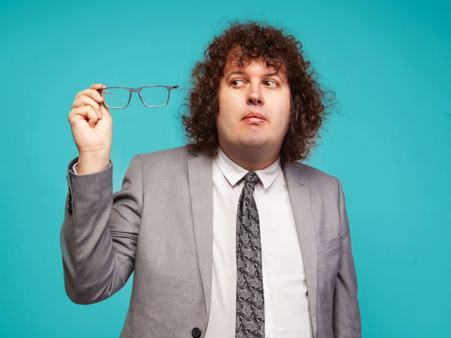 Ray in grey suit with white shirt and tie holding glasses  in the air