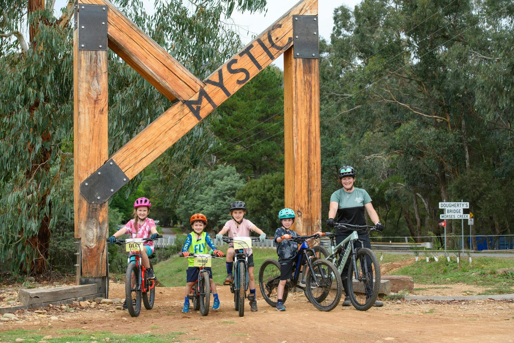 A group of young riders stand under an archway with a coach