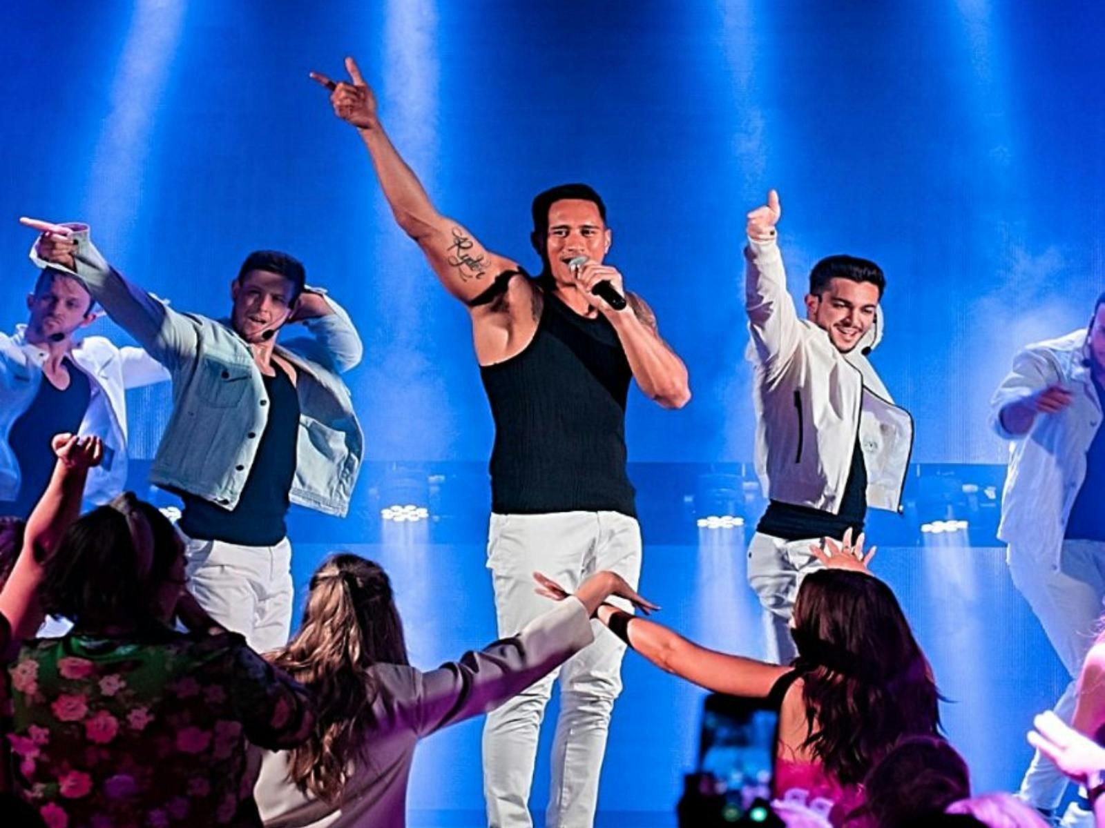 Man with black top and white pants singing on stage