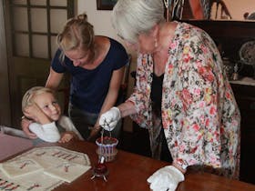 Young child listens while guide shows embroidery and silver and glass condiment containers.