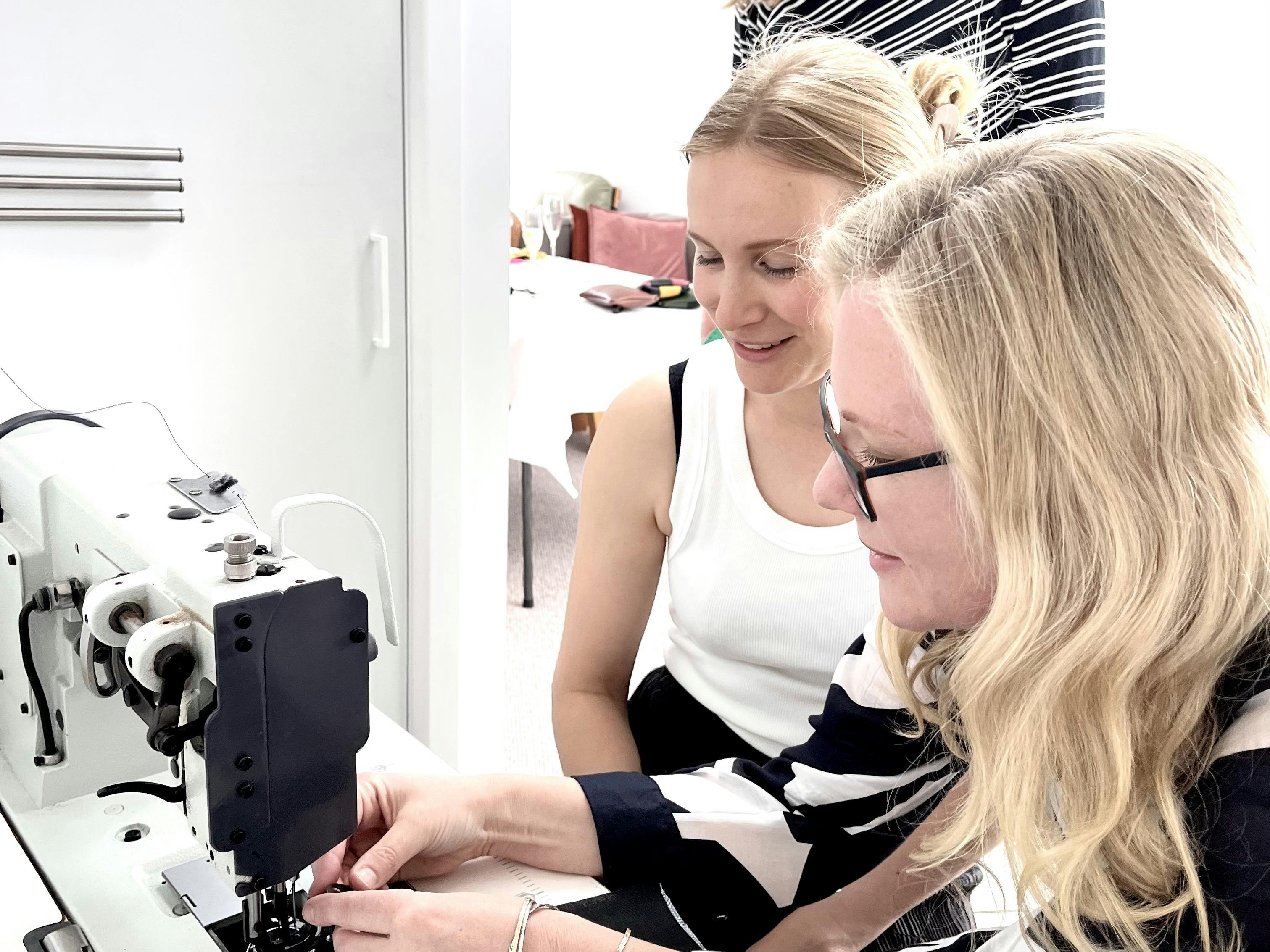 Two women working together on a sewing machine during a leather crafting workshop