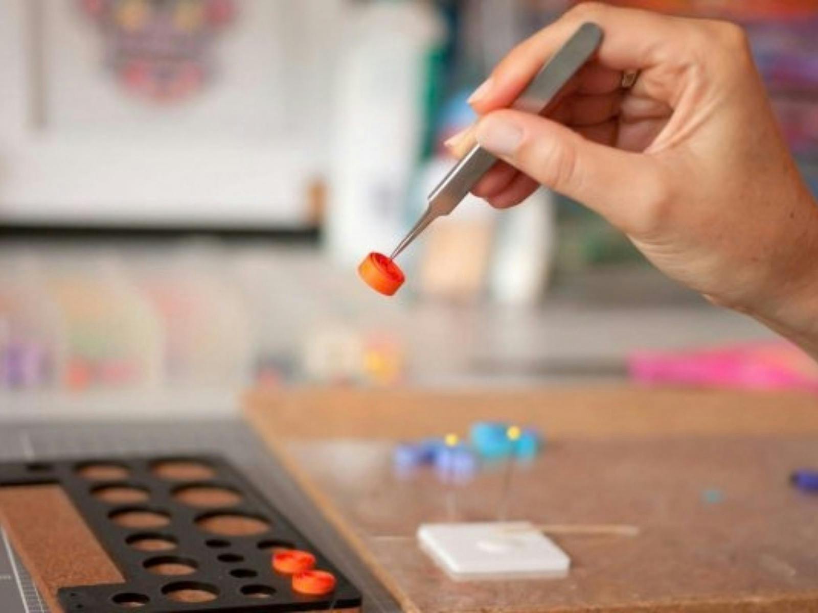 Small tweezers holding a small orange rolled circle of paper