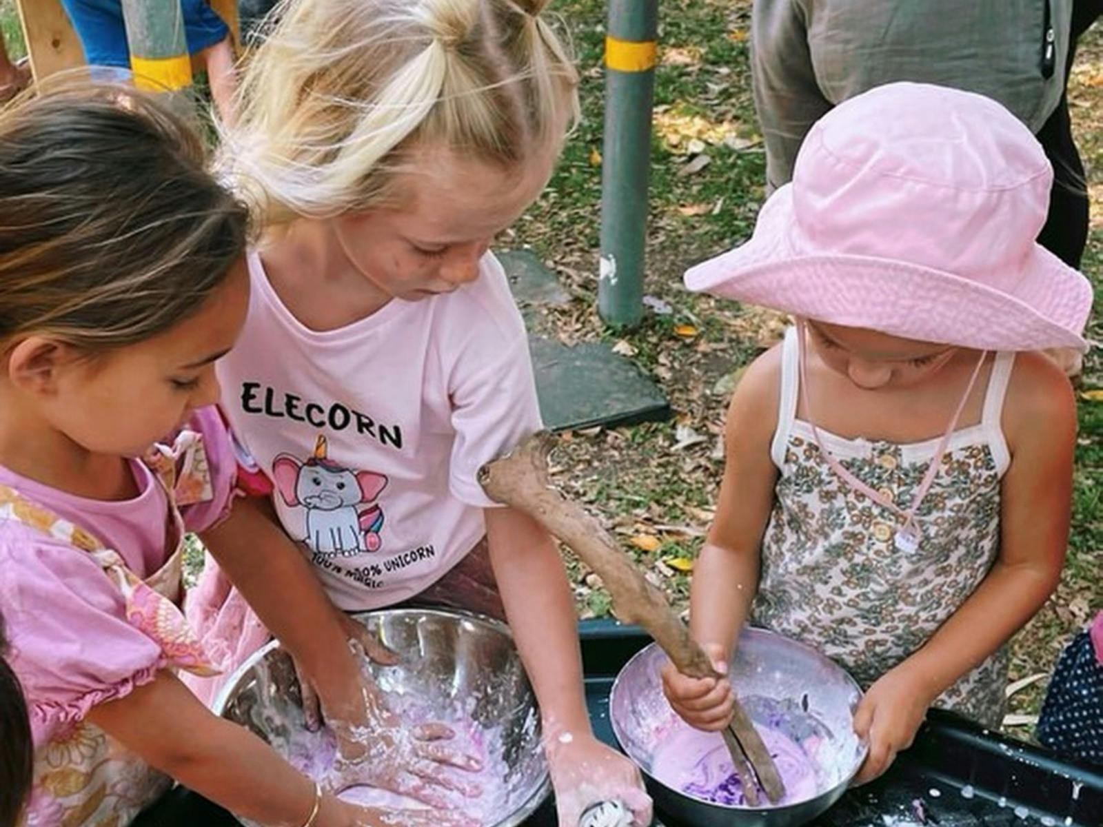 Three young girls mixing pink and purple sensory dough in metal bowls