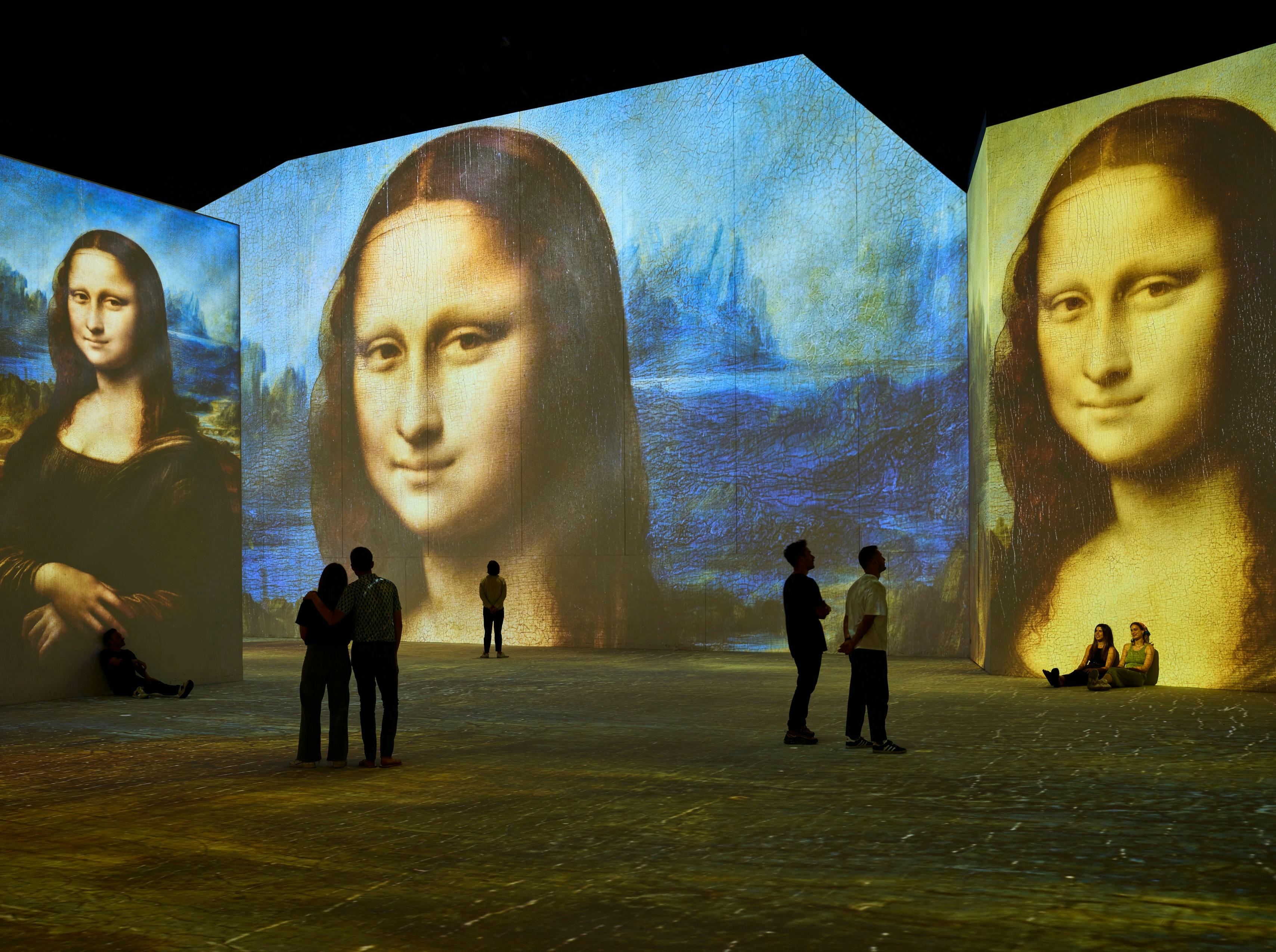 Visitors stand inside an immersive gallery as Mona Lisa projections glow across towering walls.