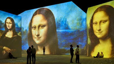 Visitors stand inside an immersive gallery as Mona Lisa projections glow across towering walls.