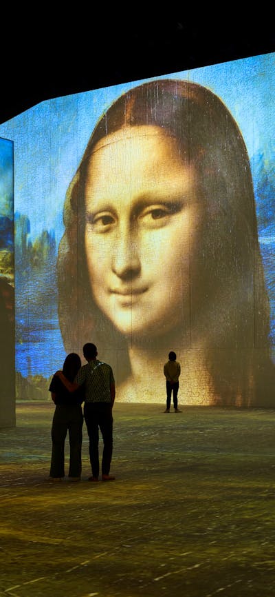 Visitors stand inside an immersive gallery as Mona Lisa projections glow across towering walls.