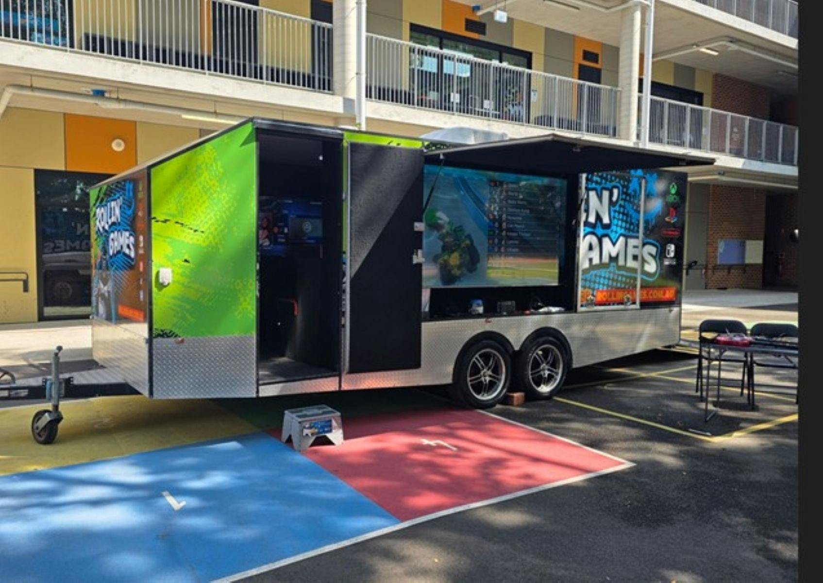 Brightly coloured large trailer in carpark, with large video game screens
