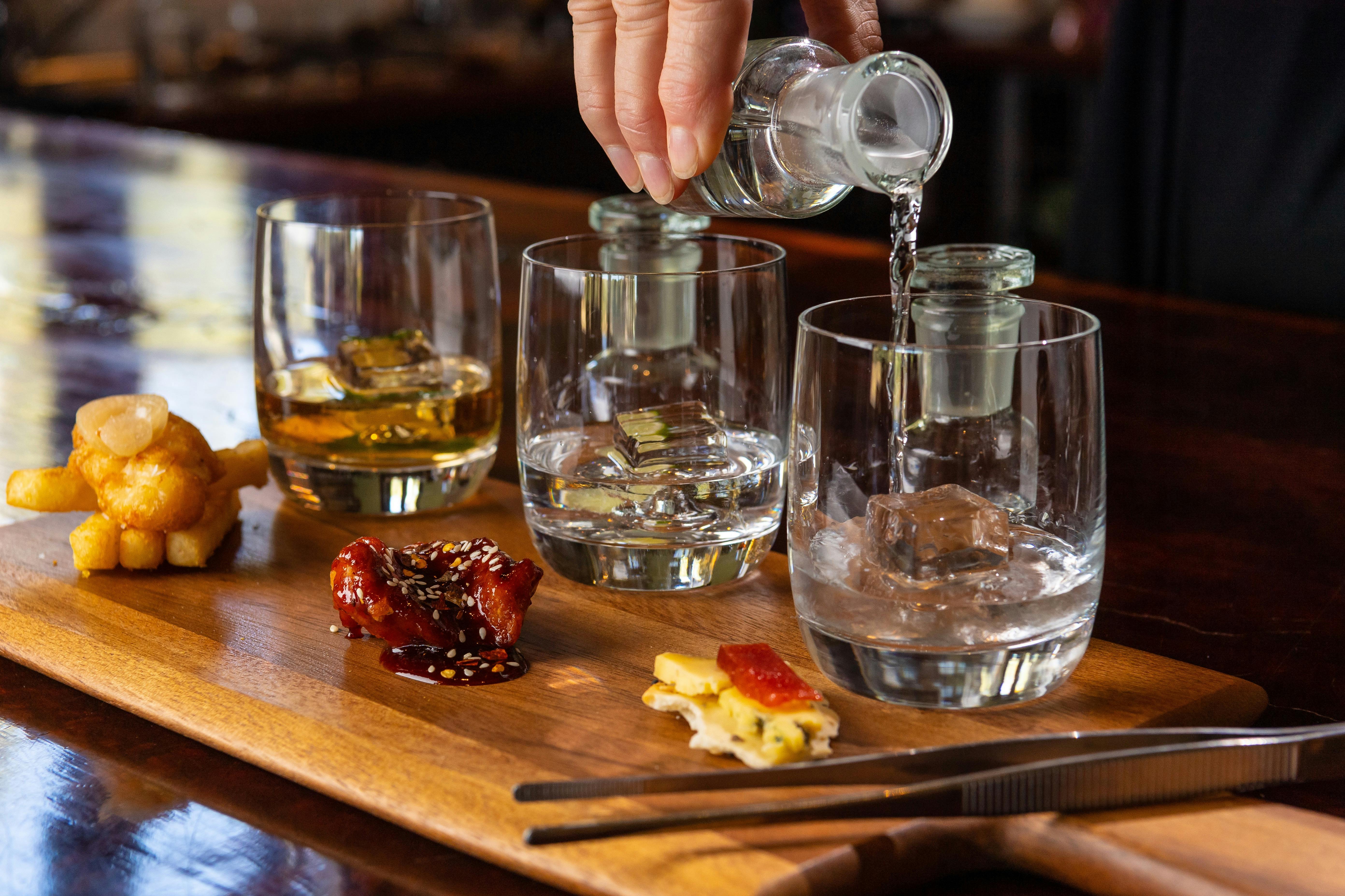 Gin being poured into tasting glasses on a board with portions of matched food