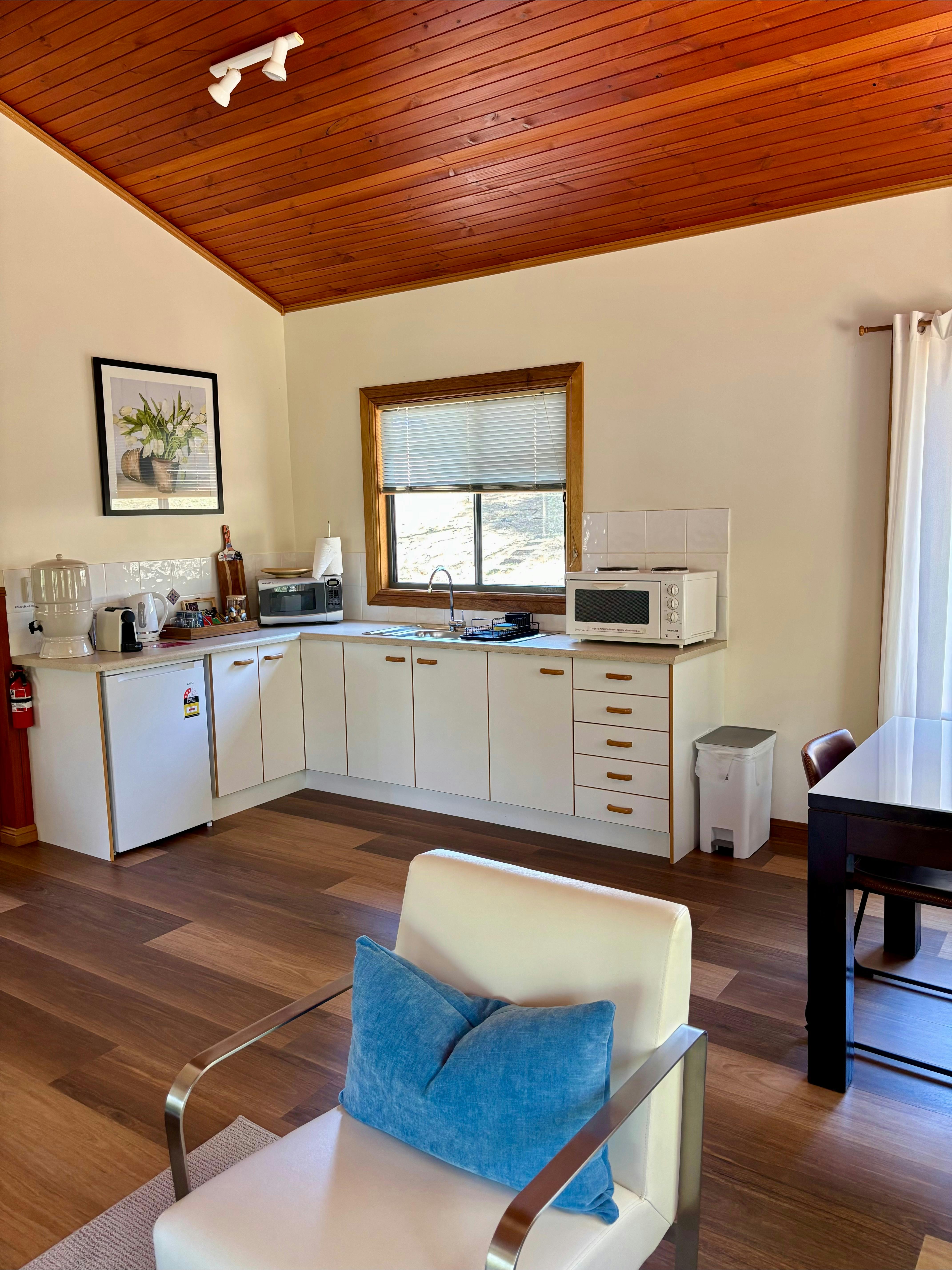 Kitchen in white with white benchtops, coffee machine and window looking out into the forest