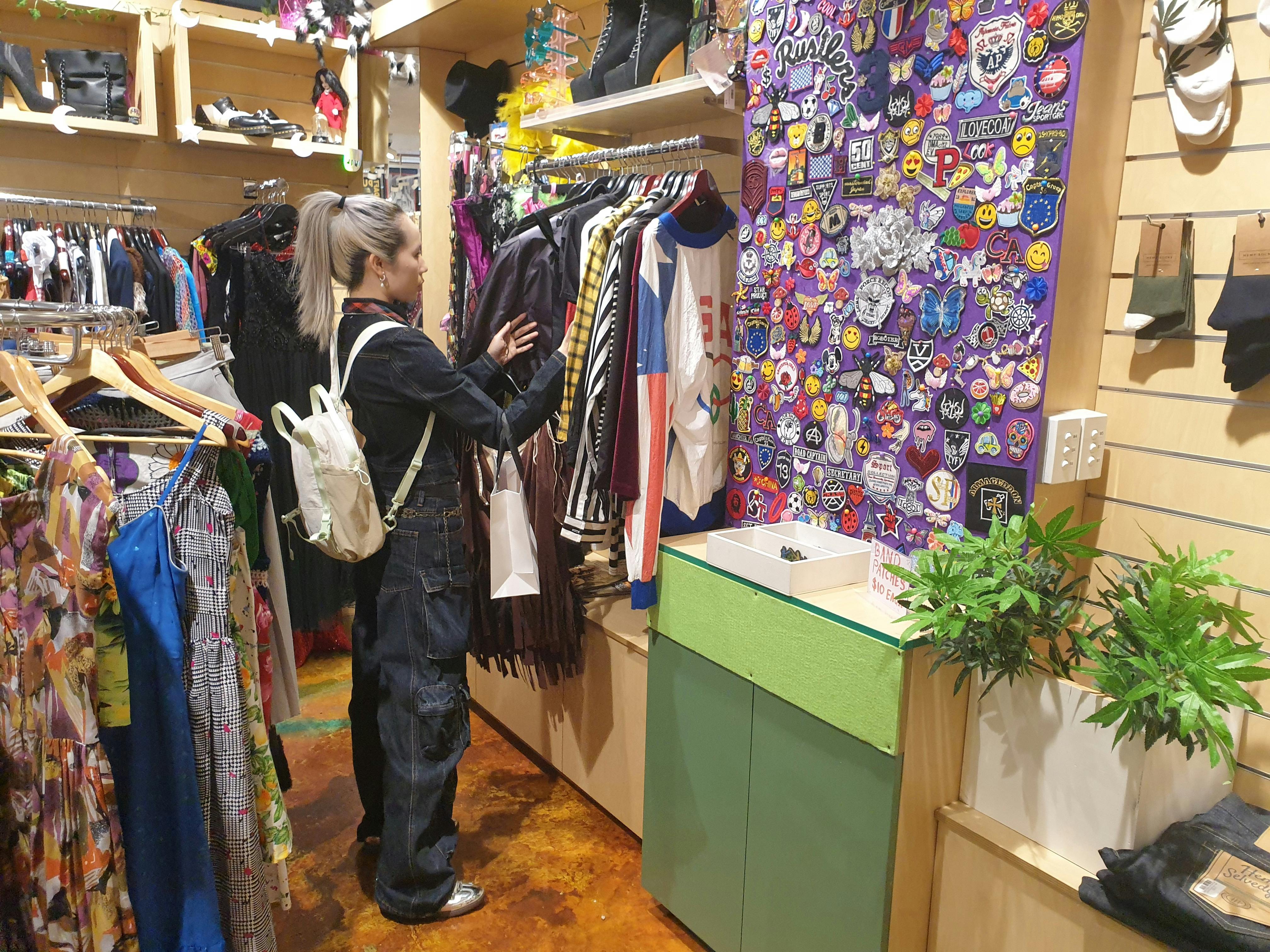 A woman looks at clothing on a wall rack surrounded by colourful items.