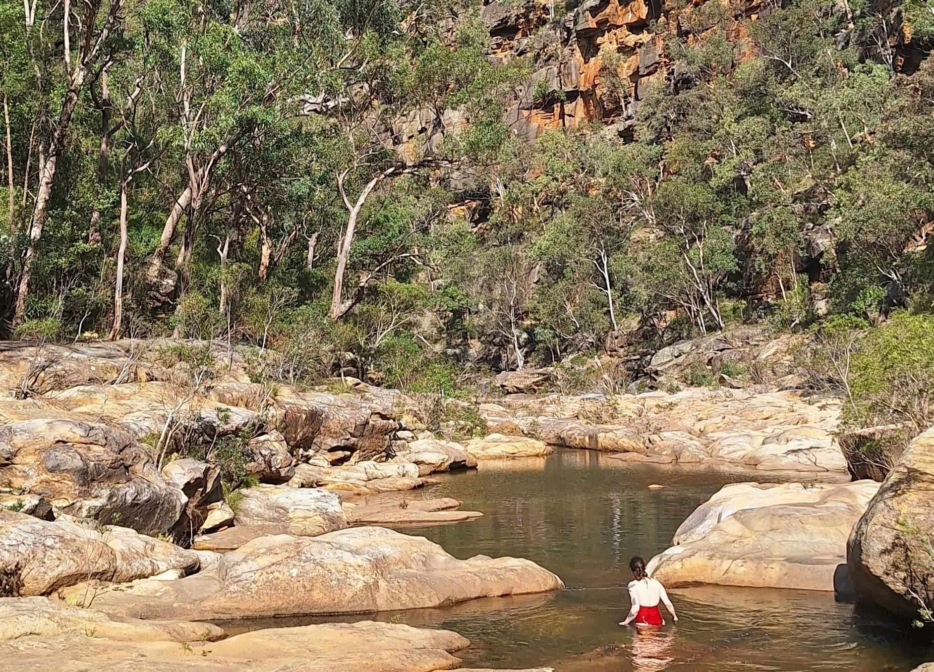 a girl wades through a pool among cliffs and bushes