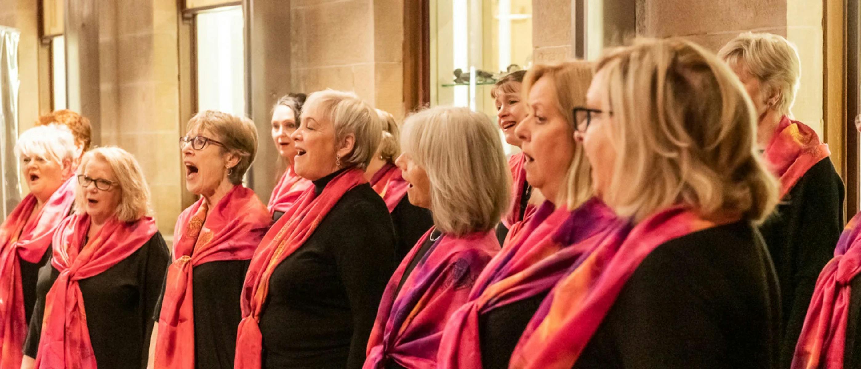 A group of women singing and wearing pink neck scarves