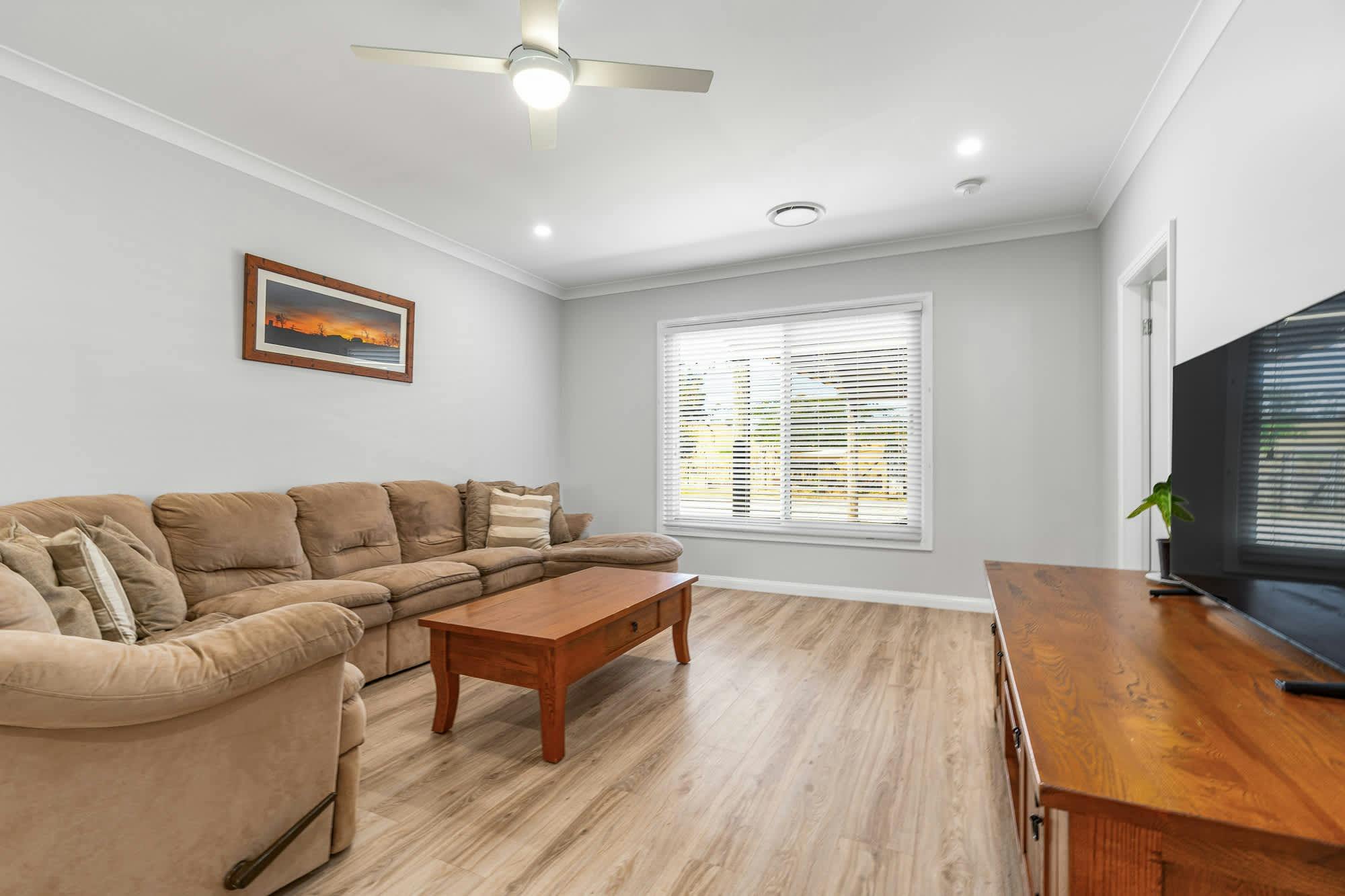 Large brown comfy couch with wooden furniture, art on walls and large flat screen tv