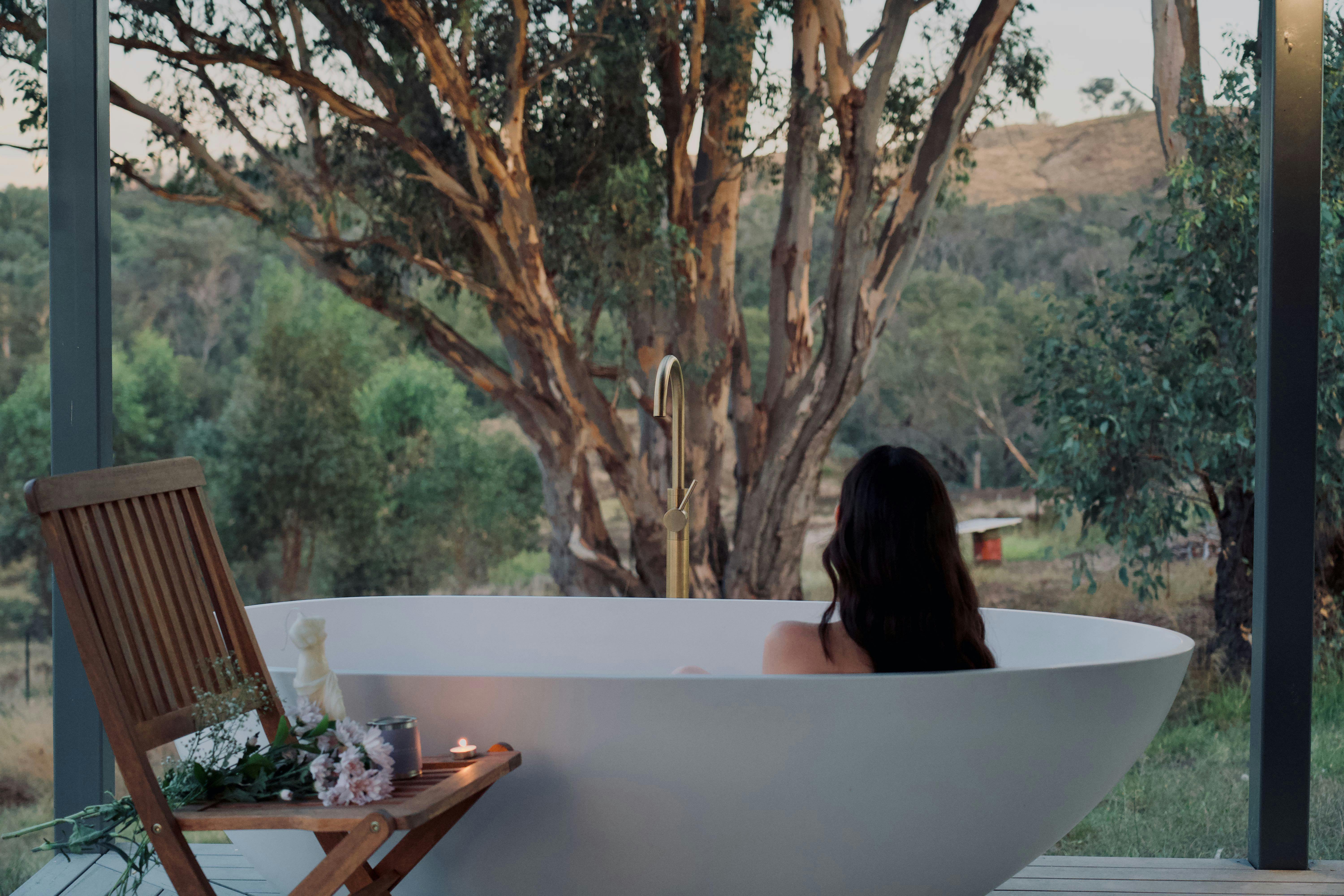 ベランダの白い浴槽の中に女性がいる。背景には巨大なユーカリの木がある