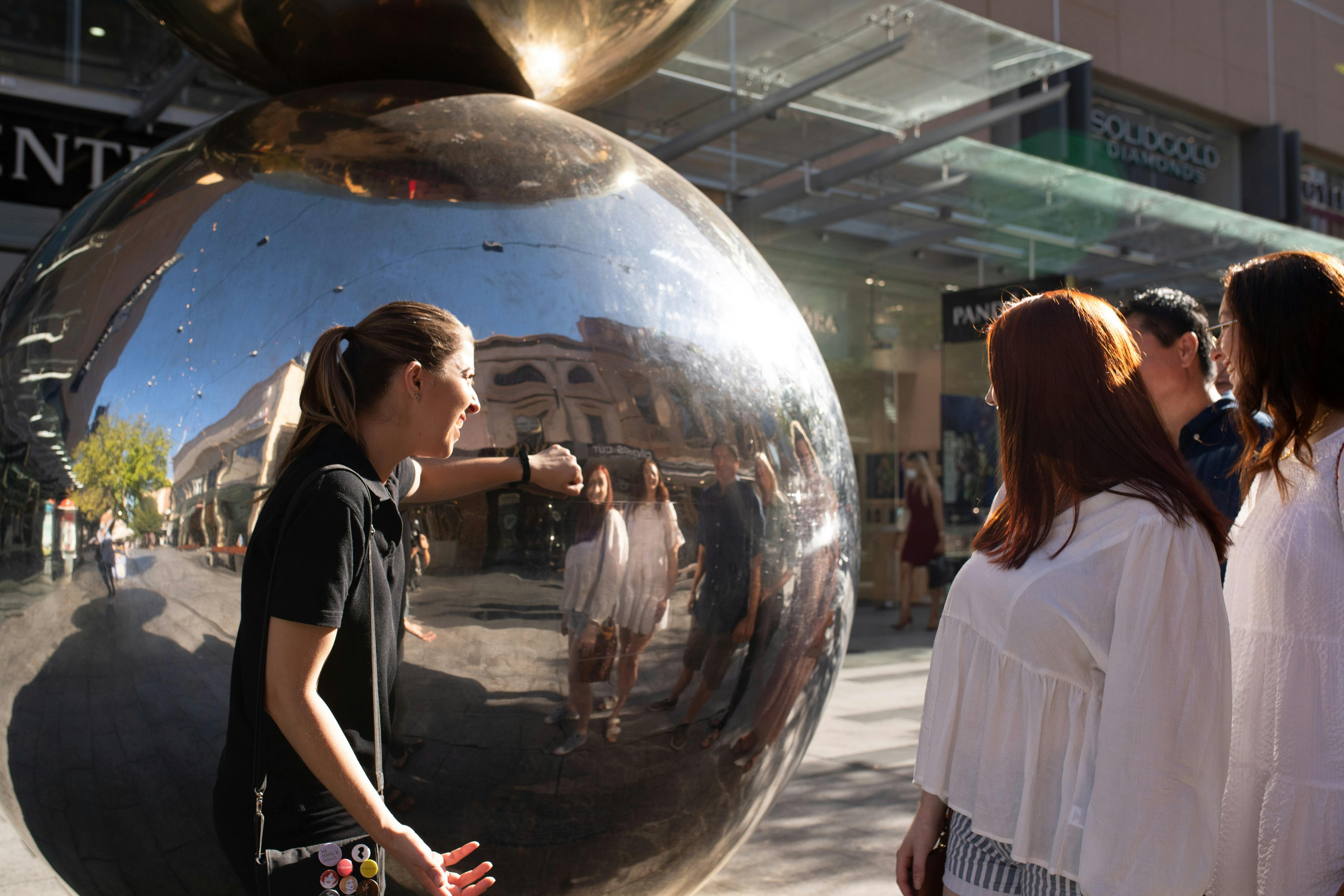 A guide knocks on a steel sculpture as a group looks on.