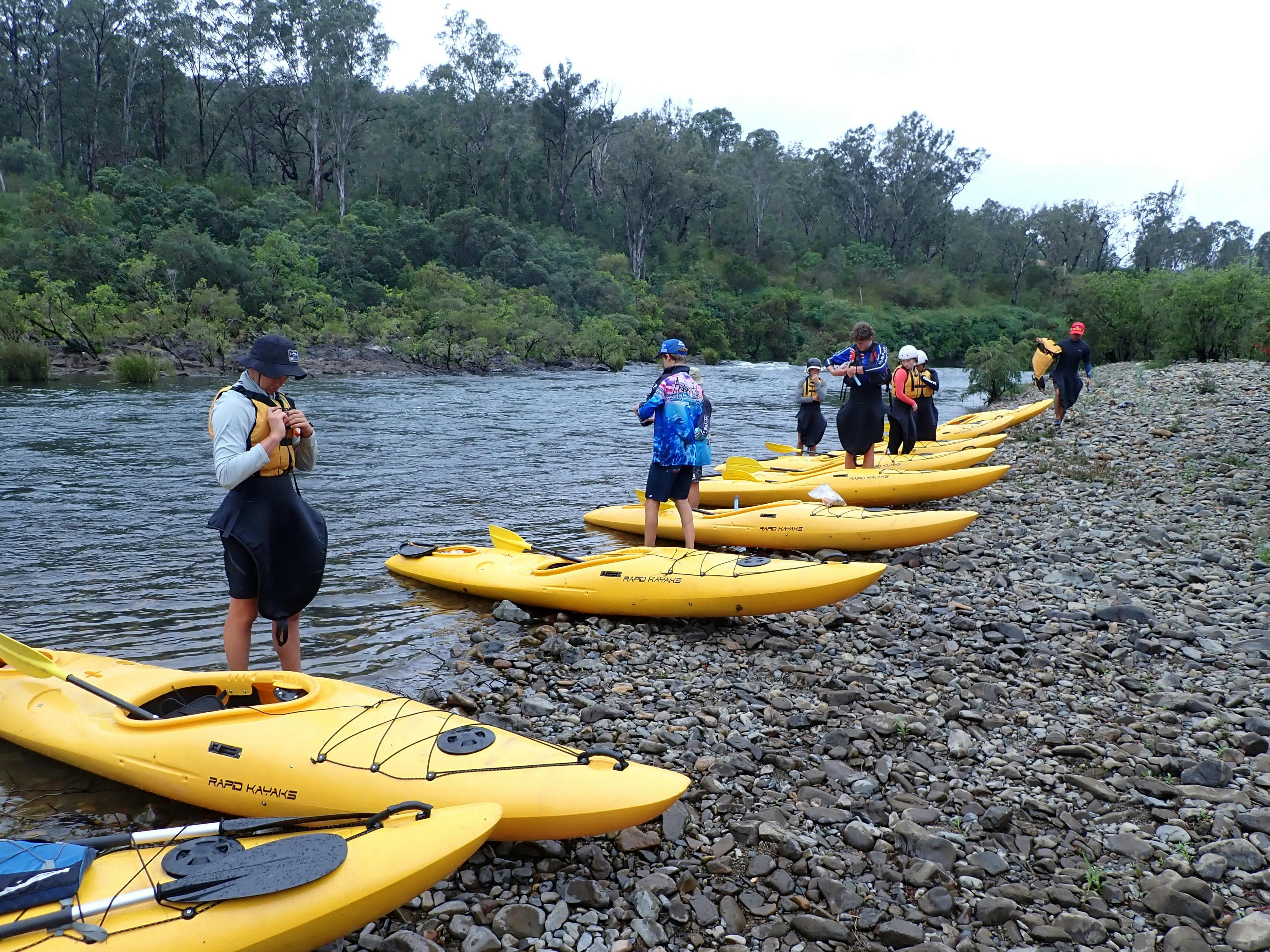 A row of Nymboida River Kayak Adventure kayaks are  lined up on the river bank