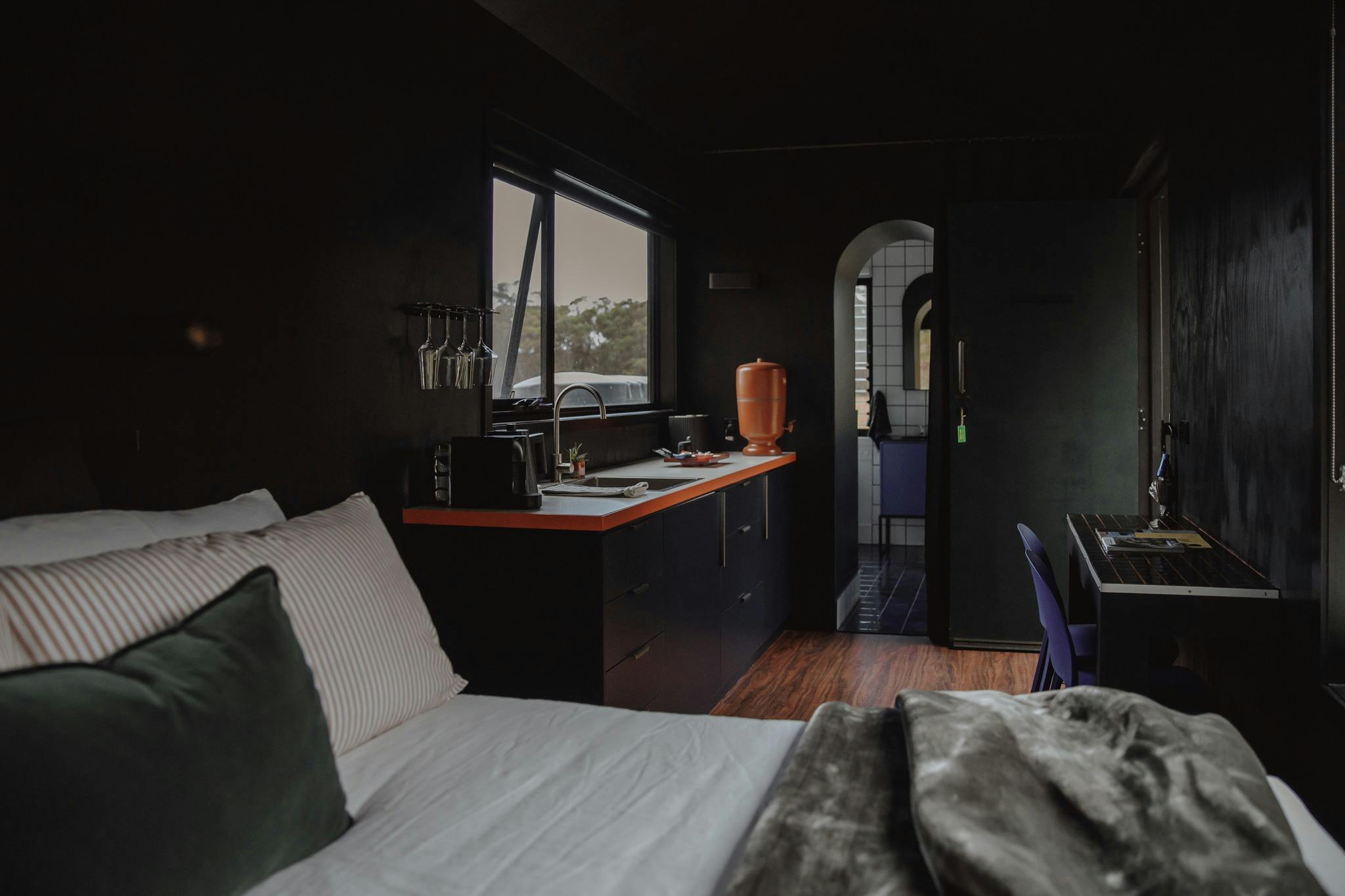A queen bed in the foreground, kitchenette and bathroom