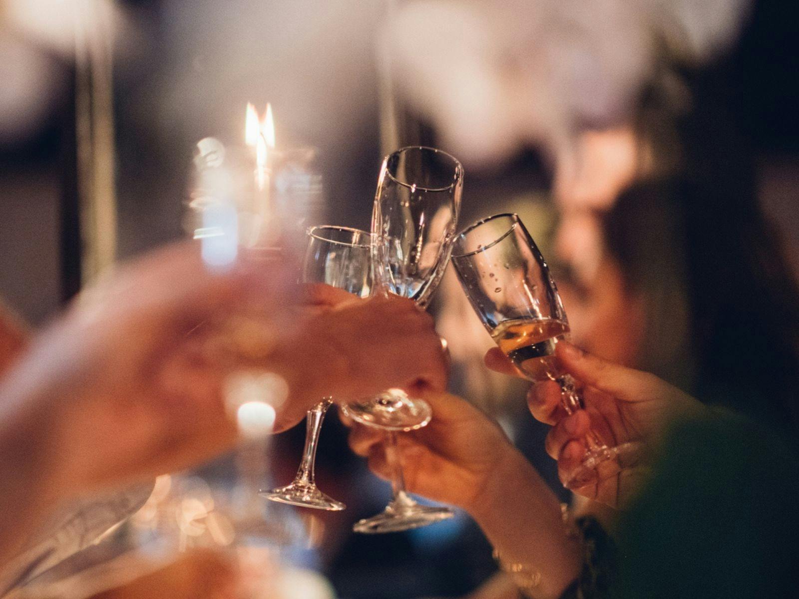 Multiple hands cheering champagne glasses together at night