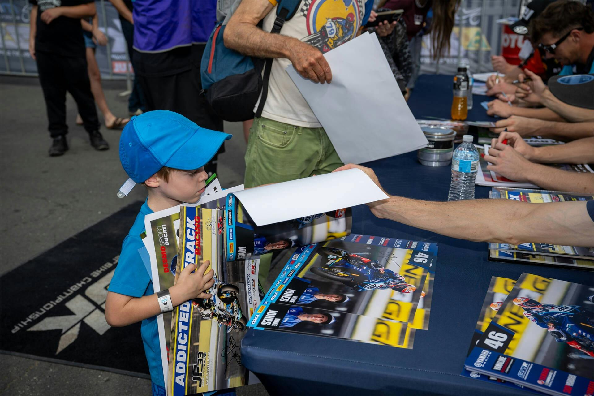 A child receiving a signed poster from riders at the signing session