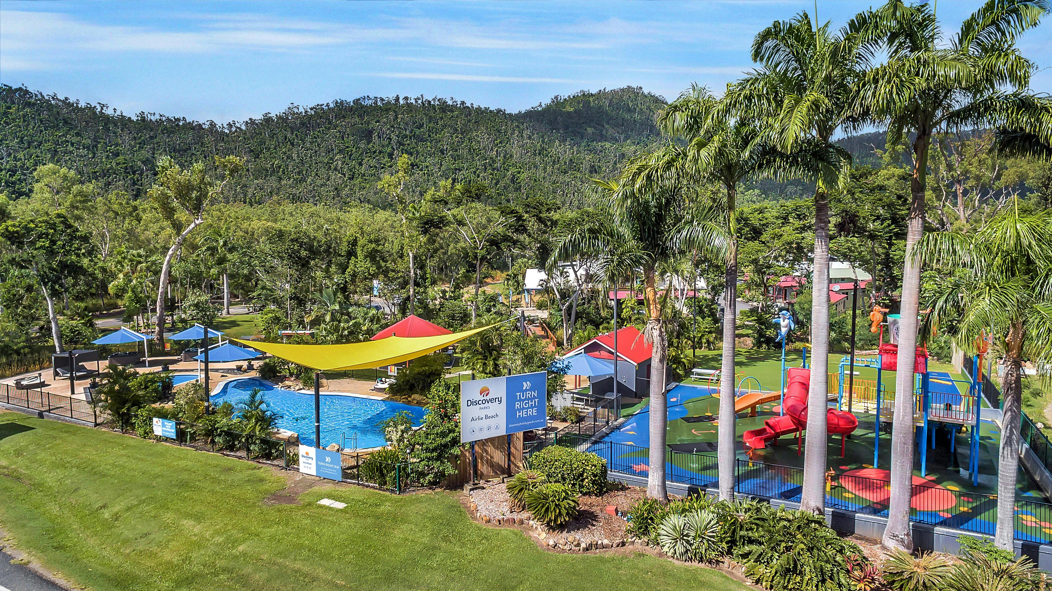 Caravan park with swimming pools surrounded by palm trees and hills at the background