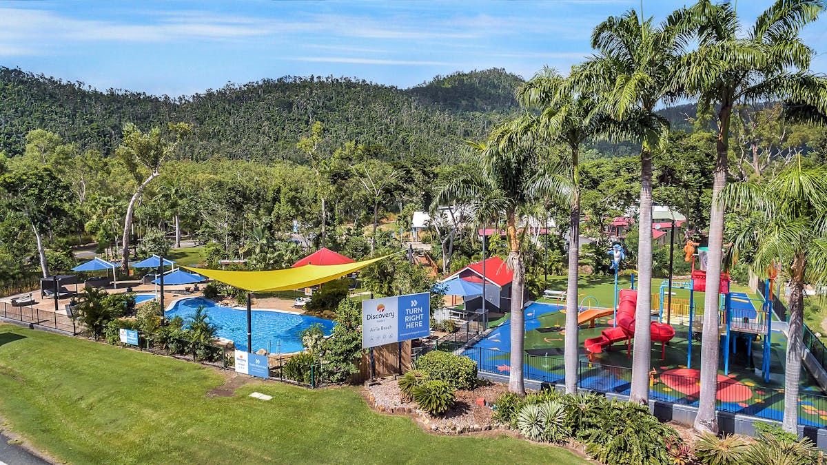 Caravan park with swimming pools surrounded by palm trees and hills at the background