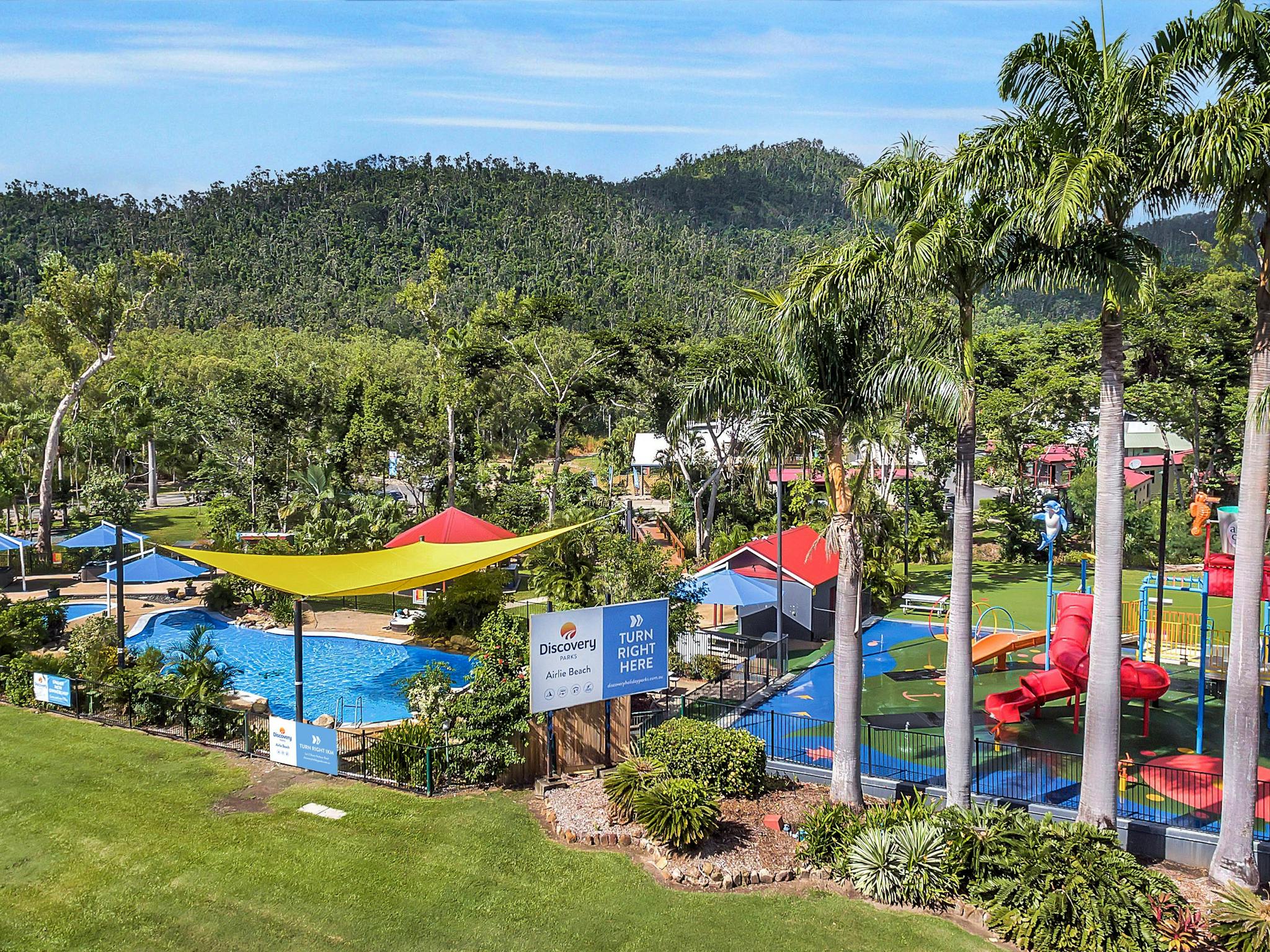 Caravan park with swimming pools surrounded by palm trees and hills at the background