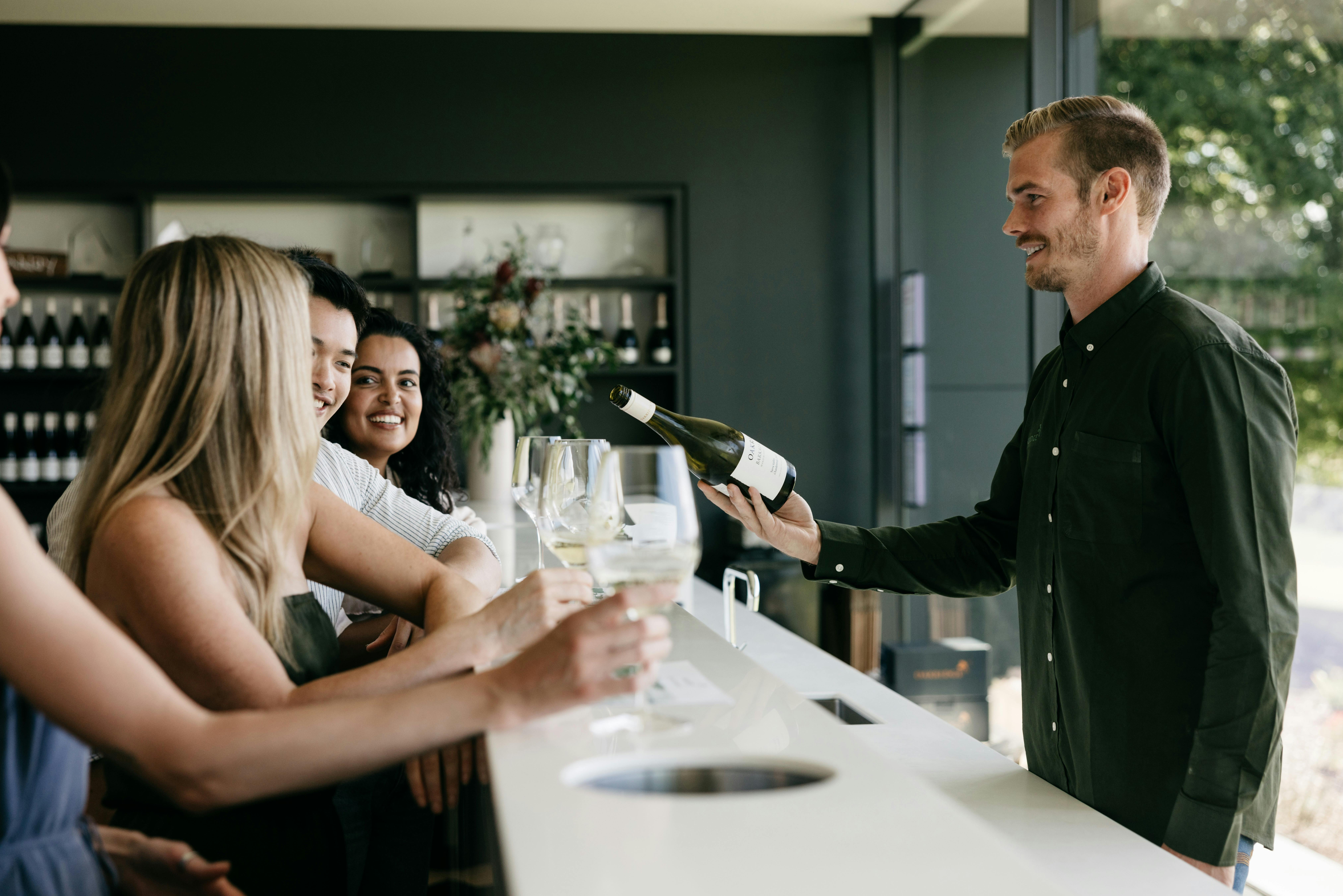 A man is serving a group of 2 women and 1 man behind Oakridge's Cellar Door bar