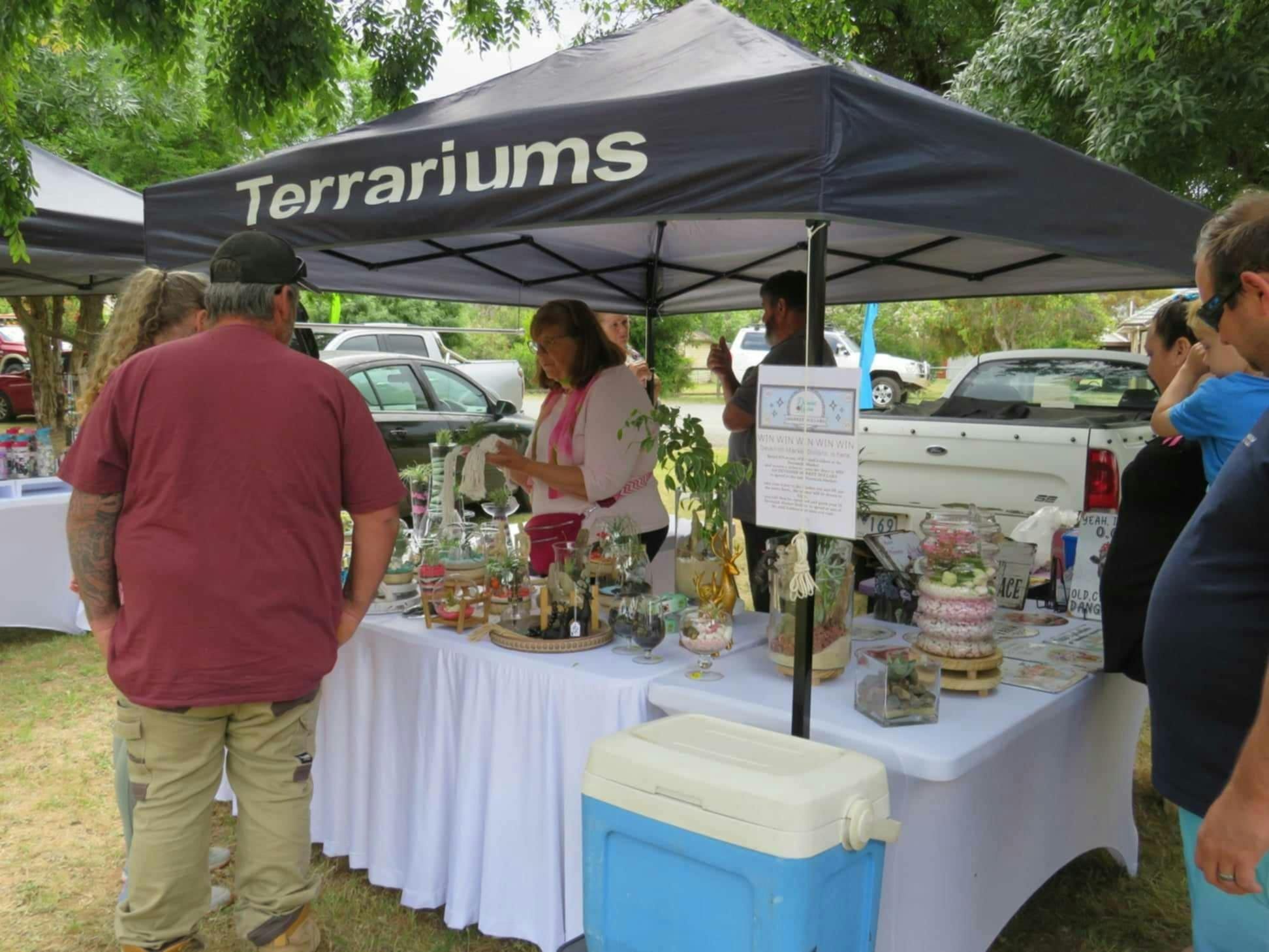 Market seller with a white top and pink scarf talks to a customer with about her product.