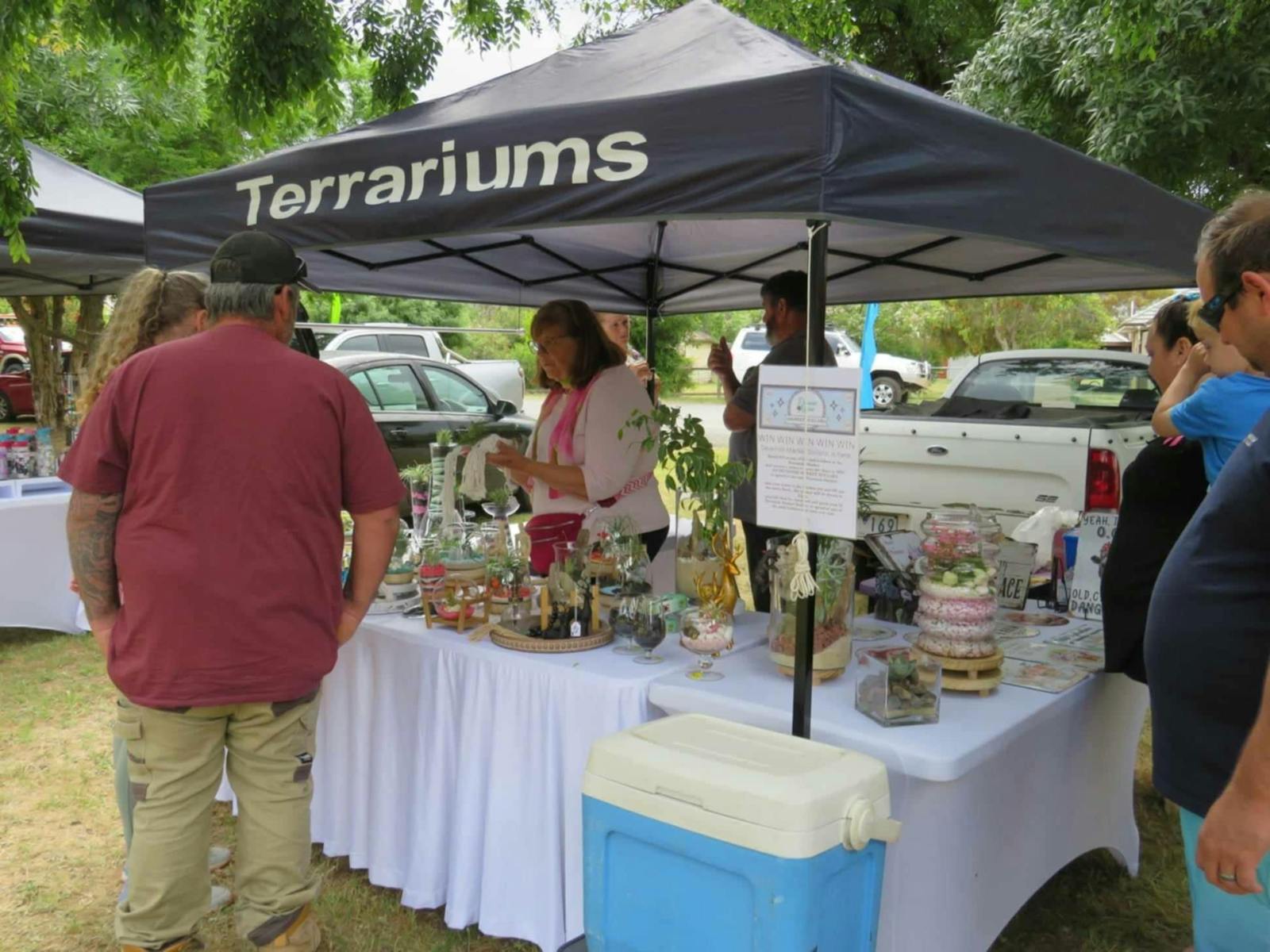 Market seller with a white top and pink scarf talks to a customer with about her product.