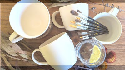 Ceramic mugs awaiting glazing with paint brushes and gin and tonic
