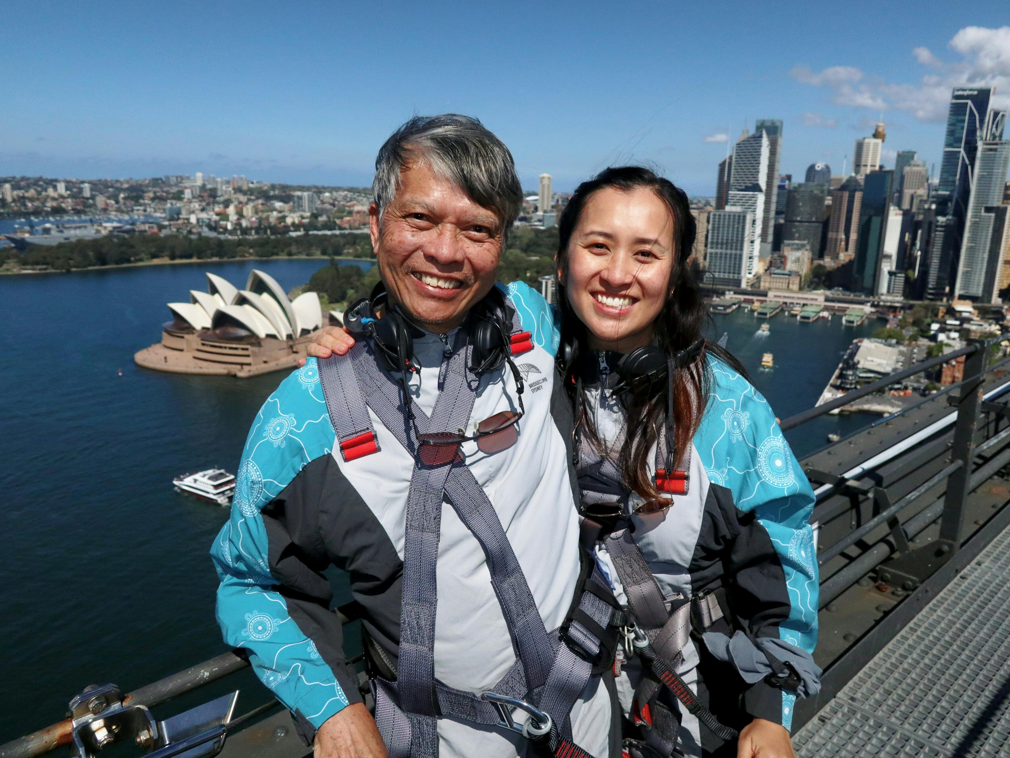 A group of Climbers walking up the upper arch of the Sydney Harbour Bridge with the Harbour behind