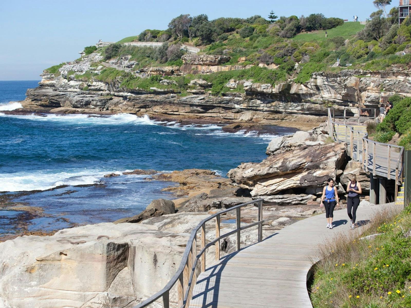 two ladies walking along boardwalk next to the ocean from bondi to tamarama in sydney