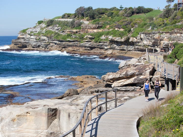 two ladies walking along boardwalk next to the ocean from bondi to tamarama in sydney