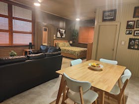 studio like accommodation with a bed, lounges, wooden blinds, lounges and kitchen table.