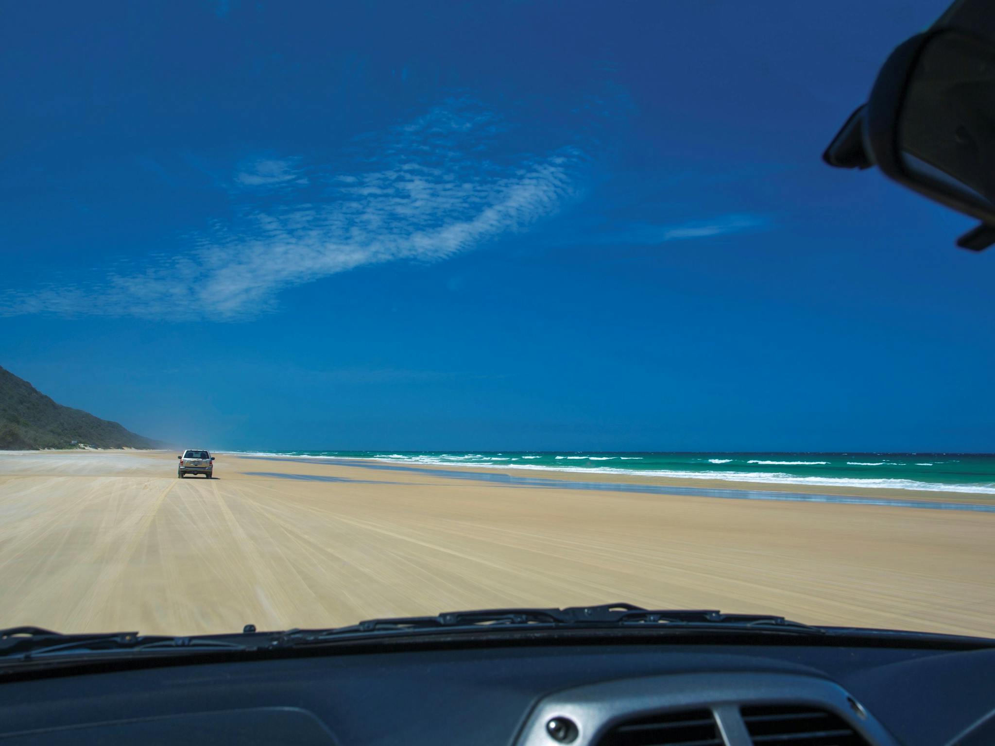 View through car window of driving along sandy beach towards headland, Cooloola.