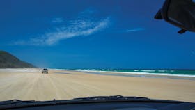 View through car window of driving along sandy beach towards headland, Cooloola.