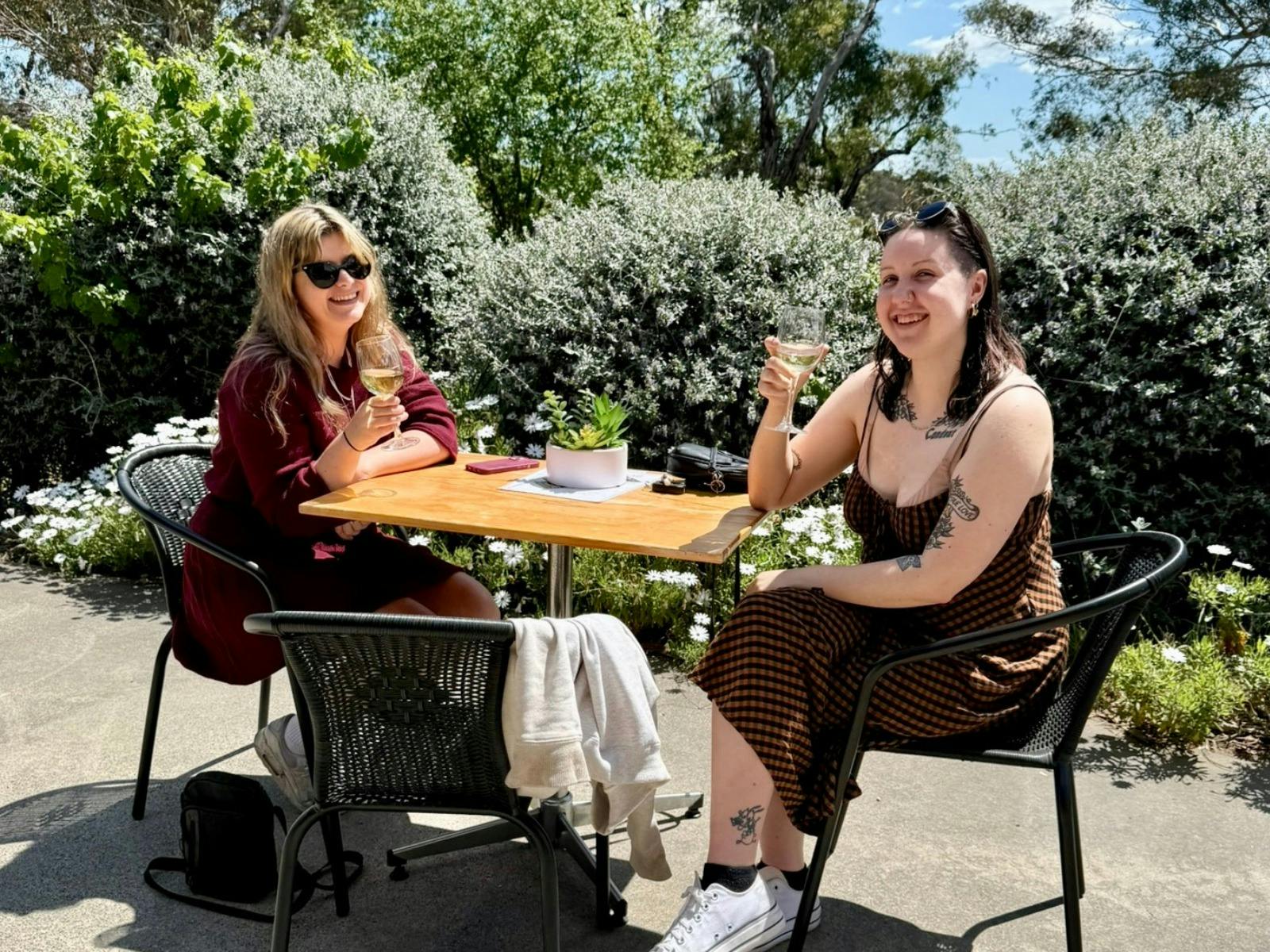 two ladies sitting at a table enjoying a glass of wine with native shrubs in the background