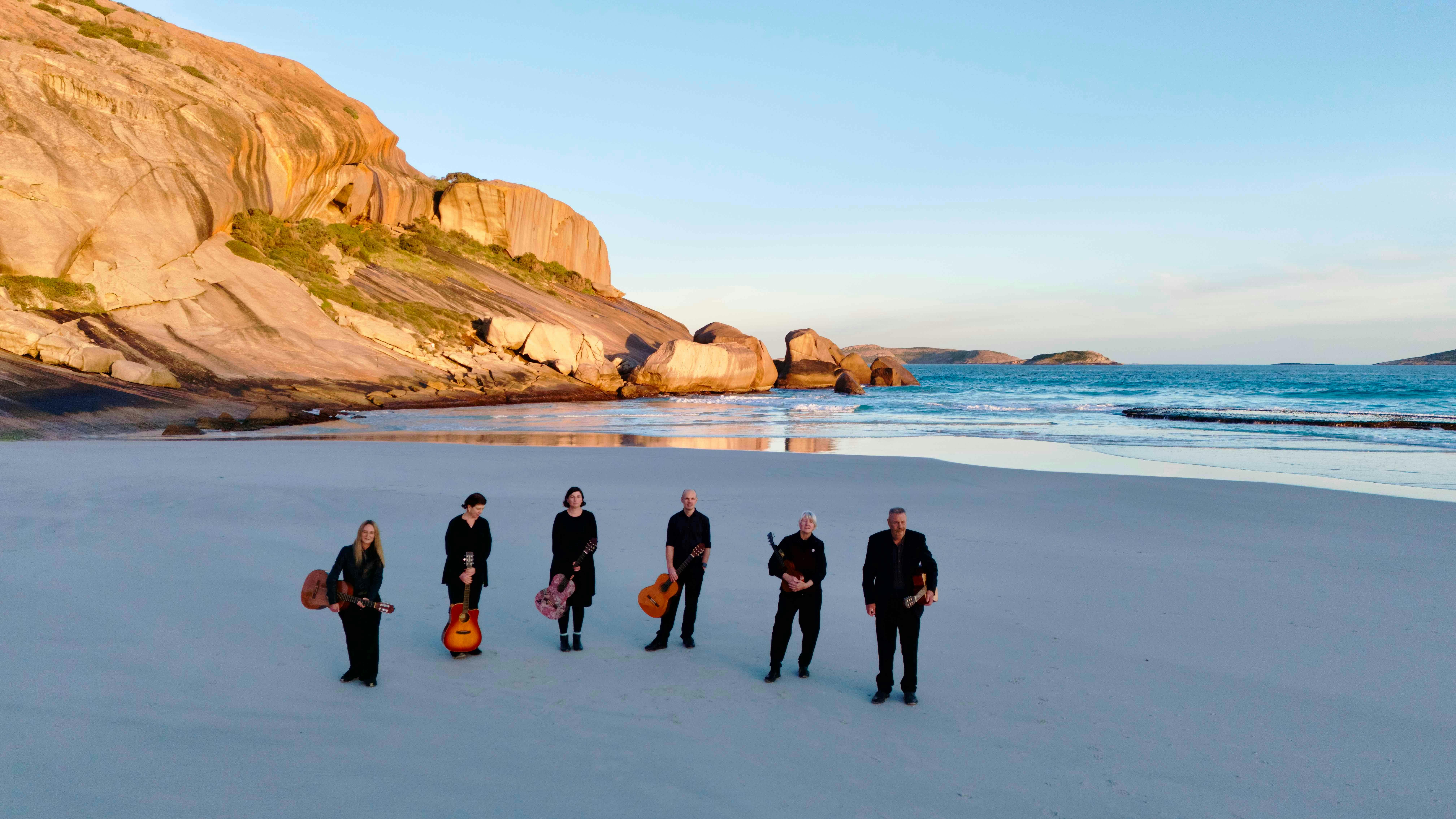 Men and women dressed in black with classical guitars on the beach.