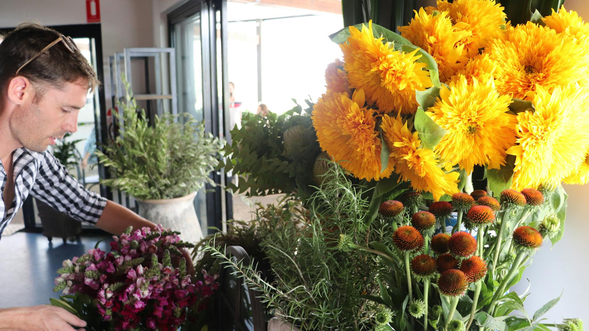 A Pantry staff member can be seen organising fresh sunflowers and snapdragons ready for purchase.
