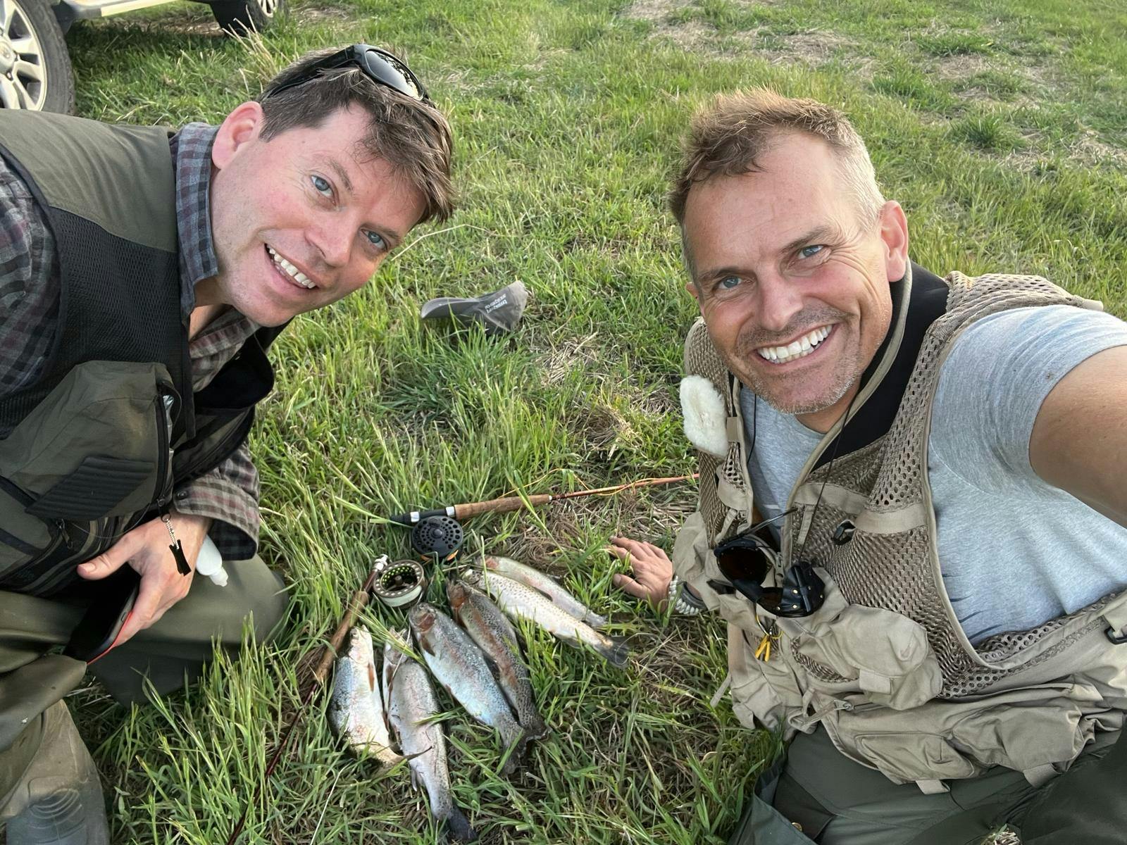 two happy fly anglers are smiling with their catch of 6 rainbow trout laid out on the river bank