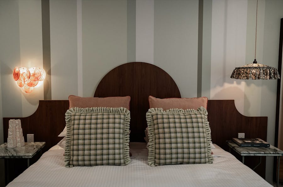 Hotel room with pillows, bed, stripes on the wall and bespoke light fixtures.