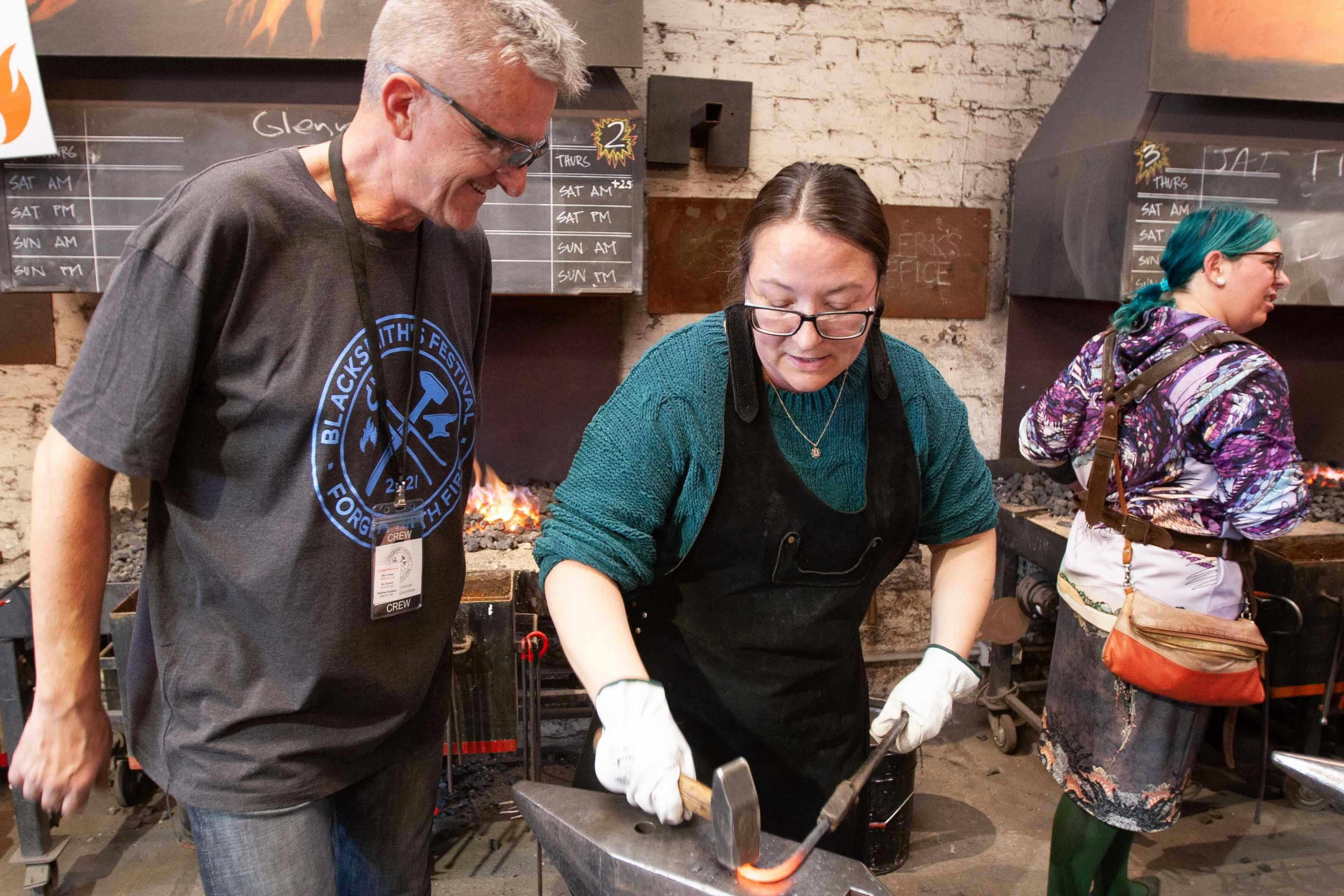 A total beginner forges an object at the festival, with guidance from helpful volunteers.