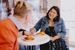 A young couple sitting at a cafe table at The Artisan Baker laughing and enjoying pastries together.