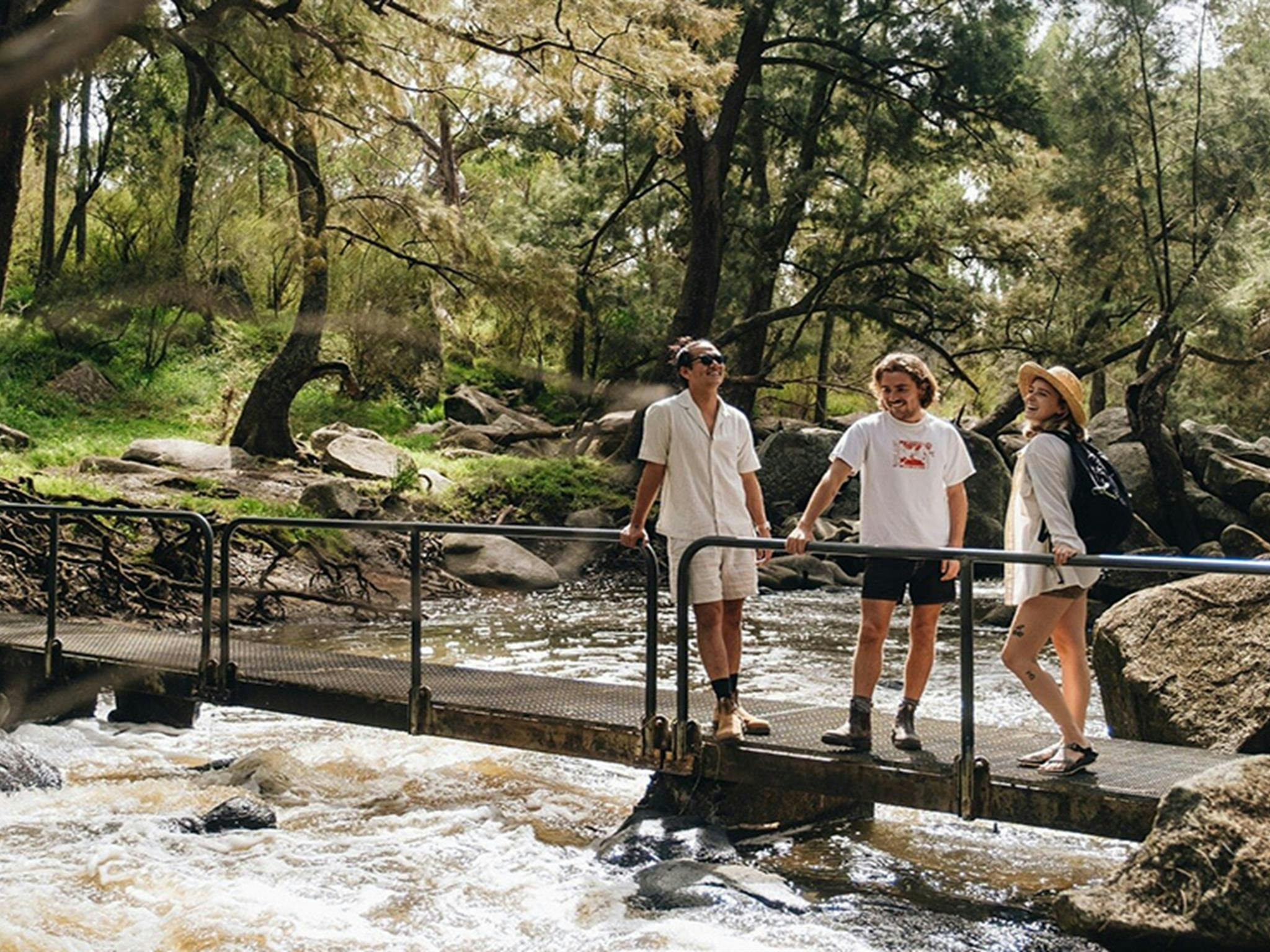 Three friends stand on a small bridge over a fast-flowing river near Blue Hole picnic area. Credit:
